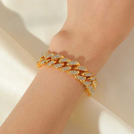 gold chain link bracelet with clear crystals on wrist against soft white fabric background