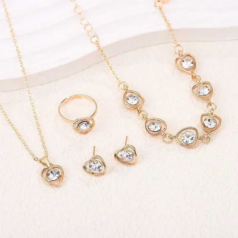 Gold jewelry set with heart-shaped clear crystals including necklace, ring, earrings, and bracelet on white surface