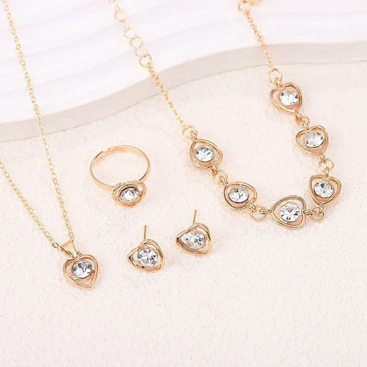 Gold jewelry set with heart-shaped clear crystals including necklace, bracelet, ring, and earrings on white background