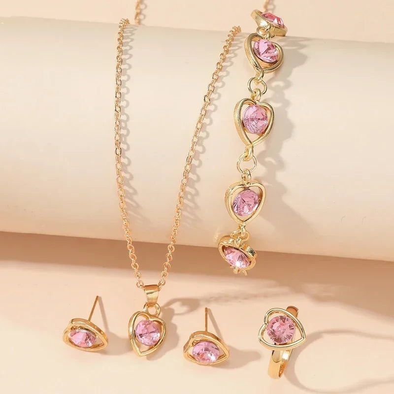 Gold jewelry set with pink heart-shaped gemstones including necklace, bracelet, earrings, and ring on beige background