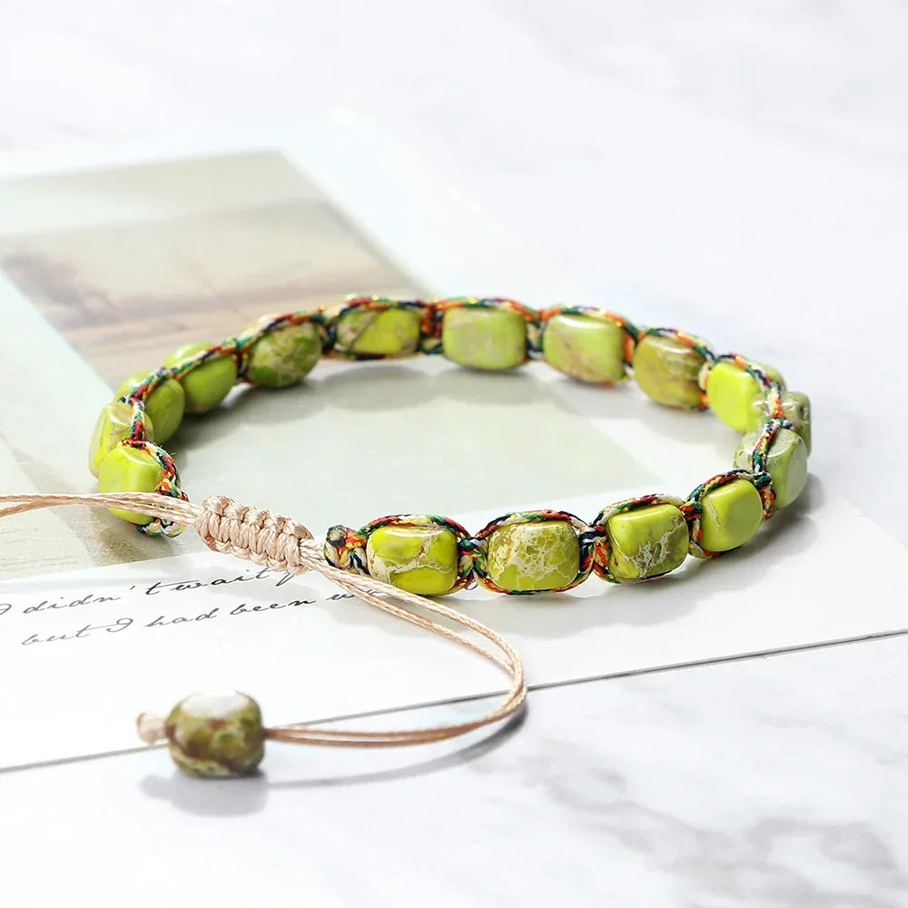 Green stone bead bracelet with multicolor woven cord and adjustable beige string on paper background