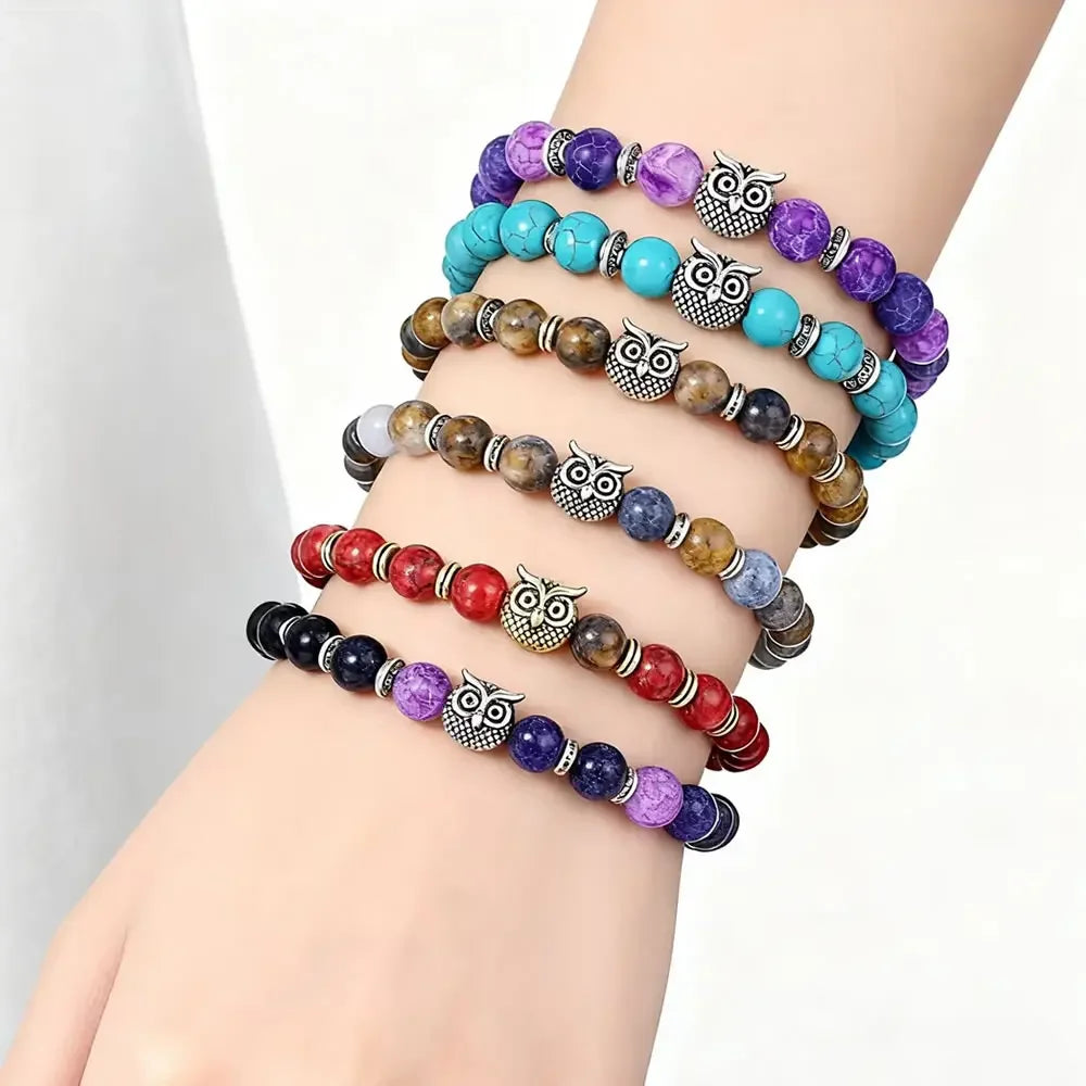 Stack of six colorful beaded bracelets with silver owl charms on a wrist